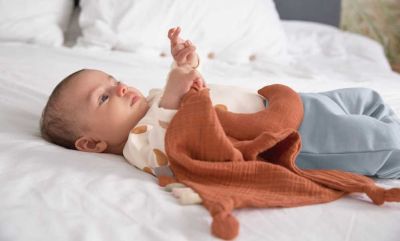 Baby spielt mit Bio Schnuffeltuch auf Bett