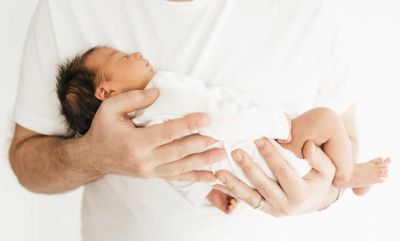 Neugeborenes Baby in Frühchenkleidung in Händen gehalten